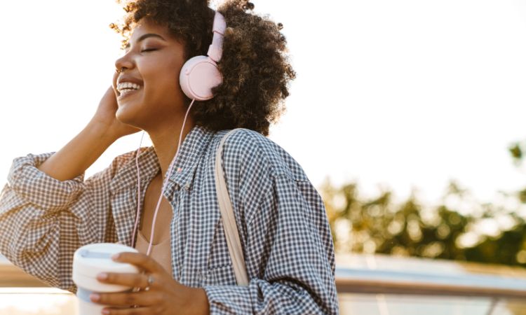 Mulher a sorrir com auscultadores ao ar livre desfrutando dos benefícios de ouvir música.