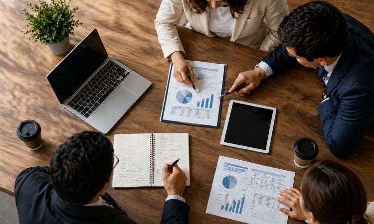 Gestão empresarial em reunião de equipa com profissionais a analisar gráficos, relatórios e dados financeiros numa mesa de escritório moderna.